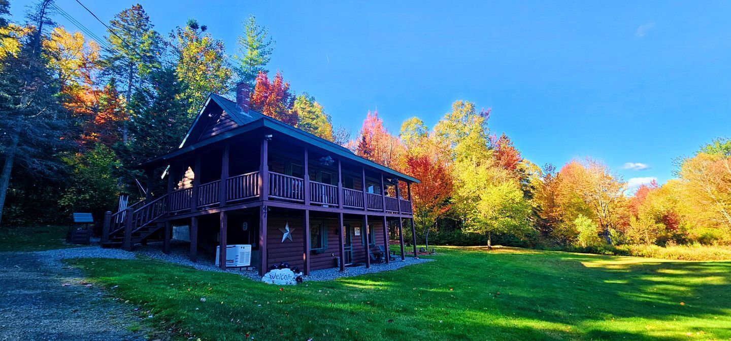 Une cabane en rondins dotée d’un porche, entourée d’arbres aux feuilles d’automne.