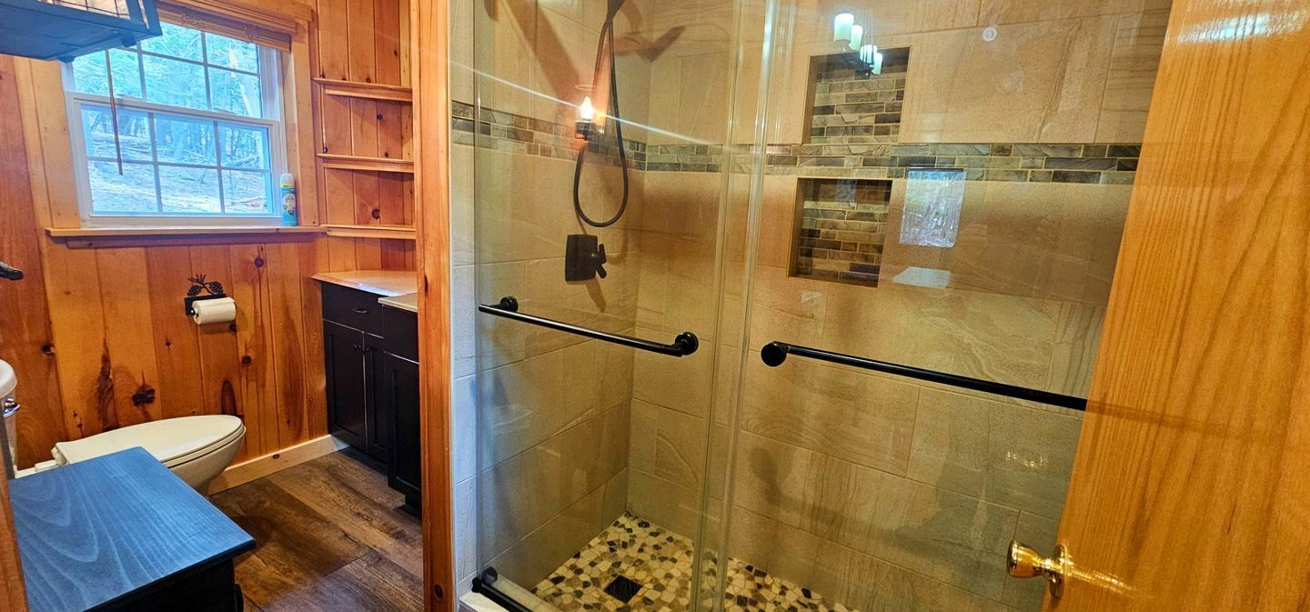 Une salle de bain avec une douche à parois de verre, des meubles en bois, des toilettes et un lavabo.