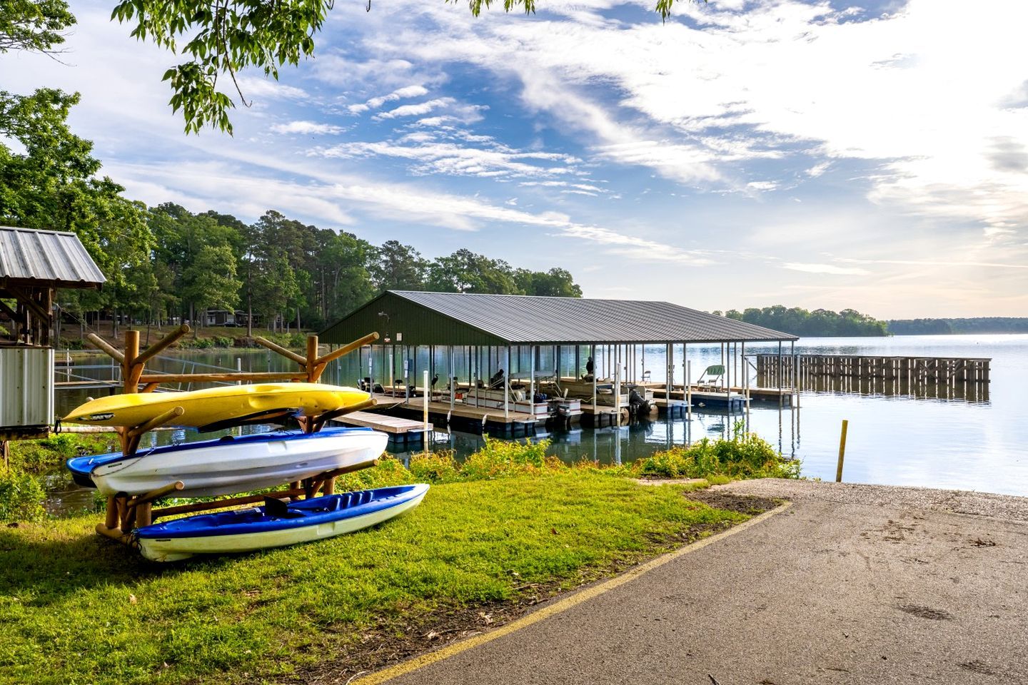 A lakeside dock with canoes, a covered seating area, and a grassy area with a path.