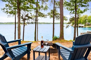 Vista de un lago con dos sillas Adirondack, una mesita y una botella de vino.