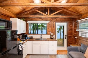 A cabin-style kitchen with a wooden ceiling, white cabinets, a stainless steel refrigerator, and a view of a lake through large windows. - Gorgeous Cabin with Beautiful Views of Toledo Bend Lake for a Relaxing Couples Getaway in Hemphill, Texas (Hemphill)