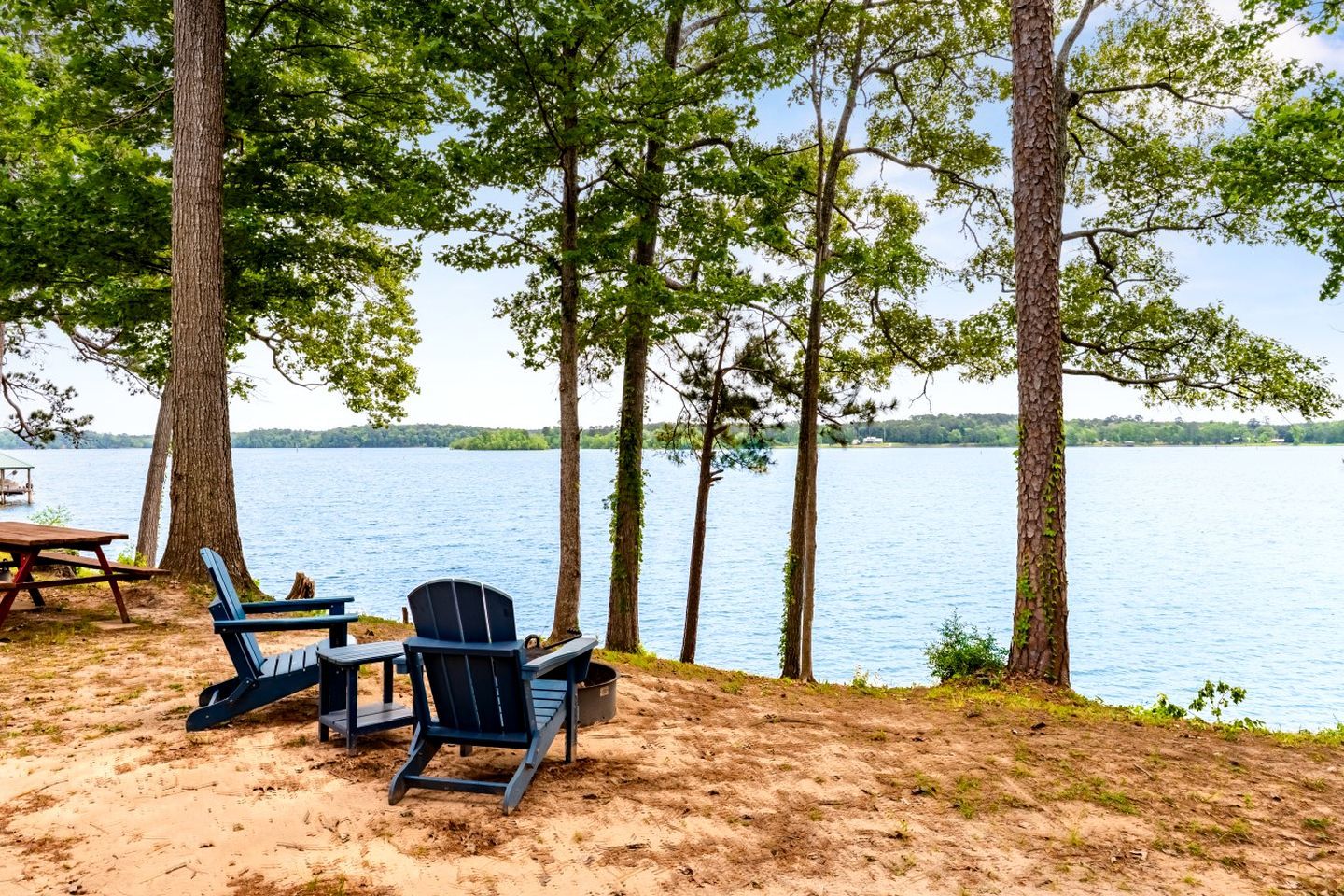 A lakeside setting with a table and chairs, surrounded by trees.