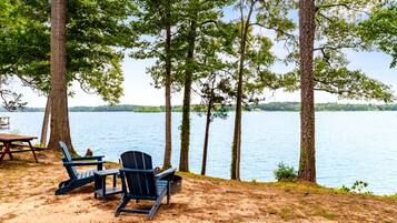 A lakeside setting with a table and chairs, surrounded by trees.