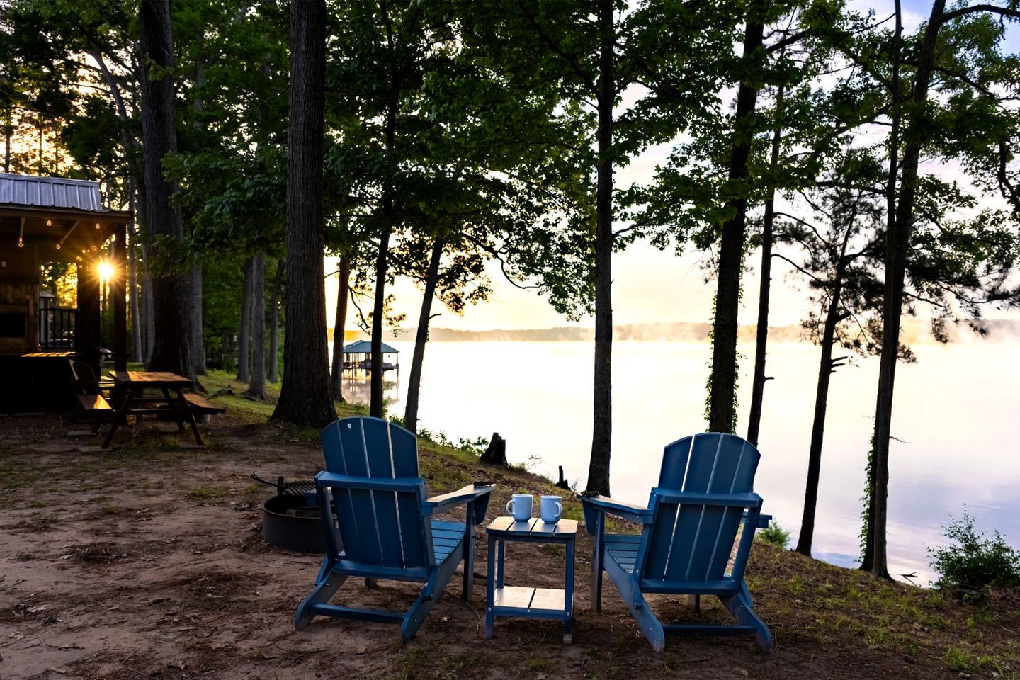 Uma cabana à beira do lago com duas cadeiras Adirondack, uma mesa pequena e área de churrasco.