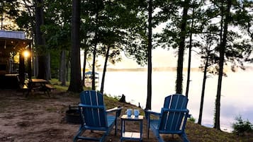 Uma cabana à beira do lago com duas cadeiras Adirondack, uma mesa pequena e área de churrasco.