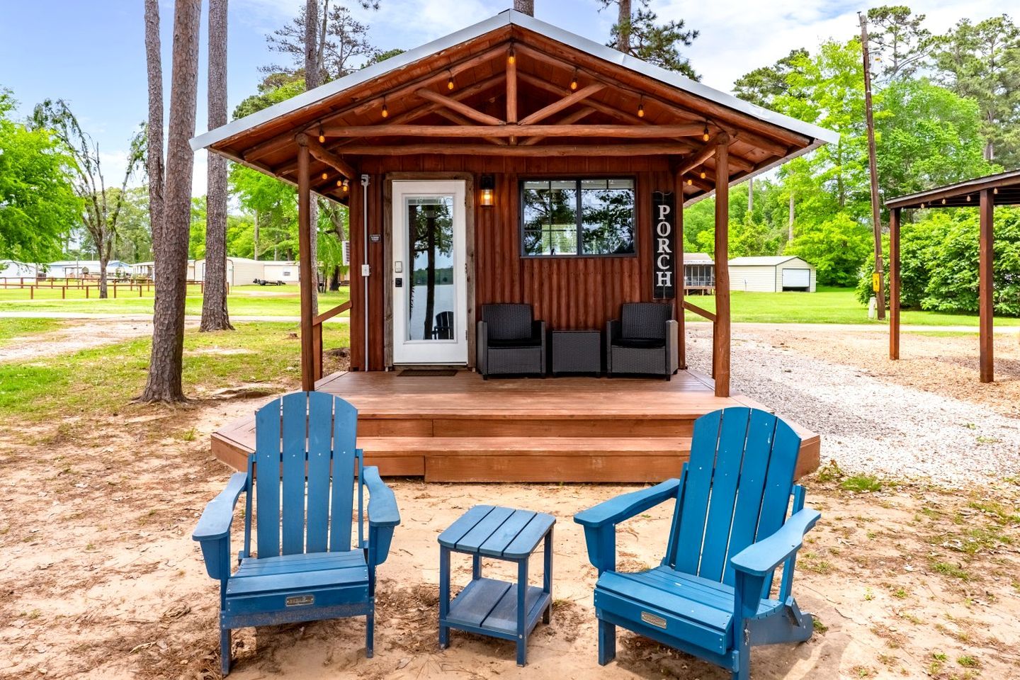 Eine Holzjagdhaus mit Veranda, zwei blaue Adirondack-Stühle und ein kleiner Tisch.