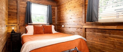 Une chambre dans un chalet en bois, avec un lit, une table de chevet, un climatiseur et une fenêtre avec des rideaux.