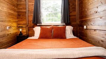 Een houten kamer in chaletstijl, met een bed, nachtkastje en lamp, en een raam met gordijnen.