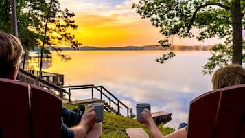 Two people seated on deck chairs overlooking a calm lake at sunset.
