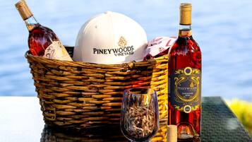 A wicker basket containing a white cap, two bottles of Piney Woods Vineyards Sangiovese, and a glass with wood shavings.