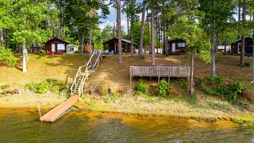 A lakeside cabin area with wooden docks, a wooden staircase, and several cabins surrounded by trees.