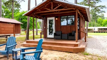 Eine Holzhütte mit Veranda, zwei Adirondack-Stühlen und Kiesgrund.