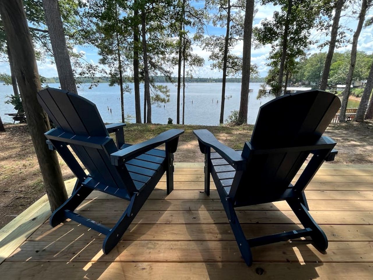 Dos sillas Adirondack en una terraza de madera con vista al lago.