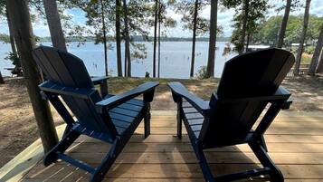 Dos sillas Adirondack en una terraza de madera con vista al lago.