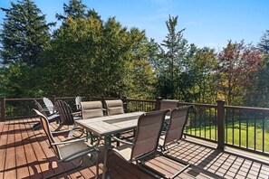 Eine Holzterrasse mit Gartenmöbeln, darunter ein Tisch und Stühle, umgeben von Bäumen.
