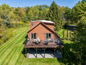 Eine Holzhütte mit einer Veranda, umgeben von einem gepflegten Rasen und Bäumen.