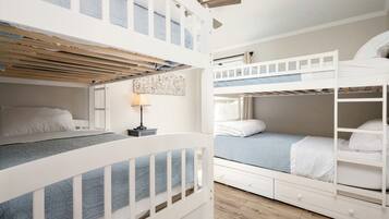 Habitación con literas, techo de madera, una mesita con lámpara y una ventana.