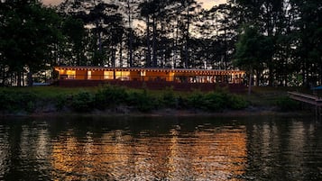 A waterfront building with a deck and outdoor seating area, surrounded by trees and a body of water.
