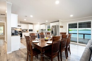 Una cocina moderna con armarios blancos, una mesa de comedor con sillas de madera y vistas a un lago a través de amplios ventanales corredizos.