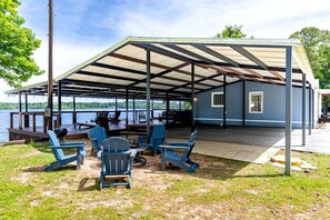 A covered outdoor seating area with Adirondack chairs, a grill, and a view of a lake. - Spacious Vacation Rental with Stunning Lake Views from the Incredible Deck for an Amazing Getaway in Sabine National Forest in Hemphill, Texas (Hemphill)