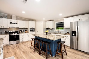 Una cocina moderna con armarios blancos, un refrigerador de acero inoxidable, una isla central con taburetes y un microondas empotrado.