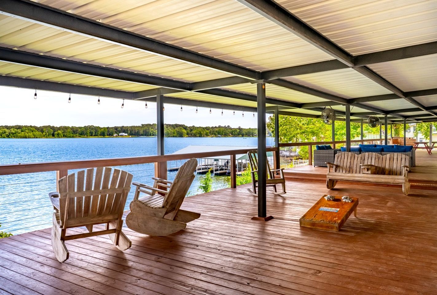 Eine überdachte Terrasse mit Holzstühlen und einer Couch, mit Blick auf ein Gewässer.