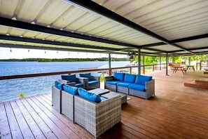 Une terrasse extérieure couverte, aménagée avec des meubles en osier, offrant une vue sur un lac et dotée d’un plancher en bois.