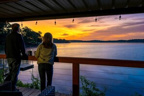A couple on a wooden deck overlooking a lake at sunset.