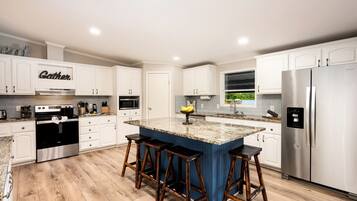 A modern kitchen with white cabinetry, a stainless steel refrigerator, a central island with stools, and a built-in microwave.