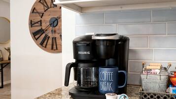 Una cafetera Keurig, una taza con la leyenda 'Coffee Break', una taza pequeña de café y un recipiente con cápsulas de café sobre una encimera de cocina.