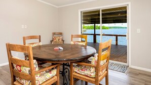Un comedor con una mesa redonda de madera y sillas, vista a un lago a través de un ventanal, y una terraza de madera en el exterior.