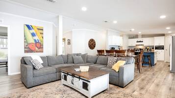 A modern living room with a sectional sofa, a coffee table, and a dining area with wooden chairs.
