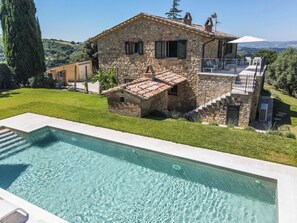 Une maison en pierre avec une piscine, un petit jardin et une vue sur la campagne.