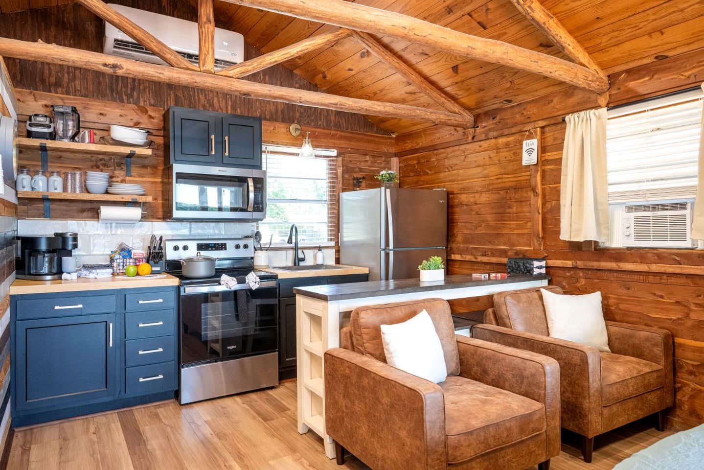A cabin-style kitchen with a stove, oven, microwave, and refrigerator. There is a wooden dining table with two chairs.