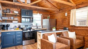 A cabin-style kitchen with a stove, oven, microwave, and refrigerator. There is a wooden dining table with two chairs.
