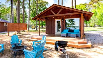 A covered outdoor seating area with a grill and Adirondack chairs.