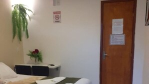 Habitación de hotel con cama, una mesita con una planta, una puerta con un letrero y suelo de baldosas.