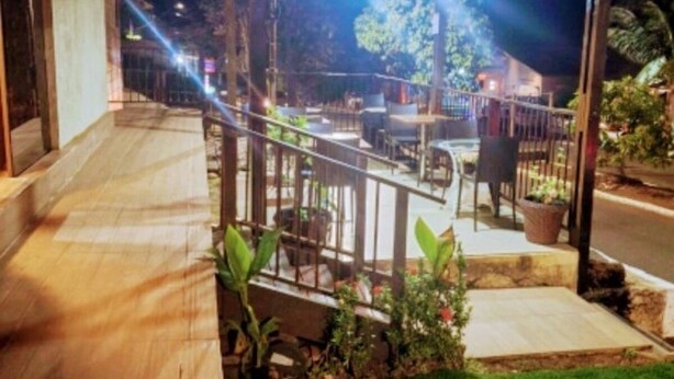 Un espacio exterior techado con una terraza de madera, un pequeño jardín y un edificio al fondo.