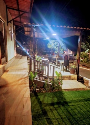 Un espacio exterior techado con una terraza de madera, un pequeño jardín y un edificio al fondo.