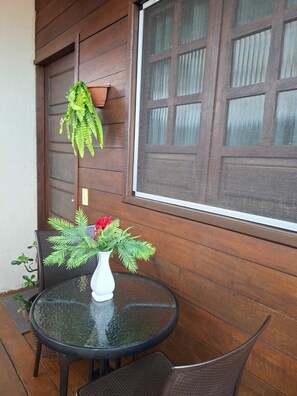 Ein runder Glastisch mit Korbstühlen, einer weißen Vase mit Grünpflanzen und roten Blumen sowie eine Holztür mit Fenster.