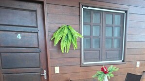 Una puerta de madera con un número, una ventana, una pequeña mesa con sillas y una planta en maceta.