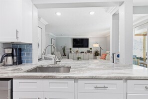 A modern kitchen with a built-in sink, a coffee maker, and a flat-screen TV mounted above the counter. - Spacious 3BR Condo in Gated St. Petersburg Community with Private Beach (St. Petersburg)