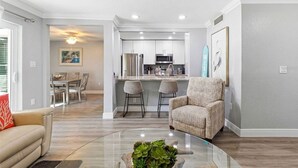 Una sala moderna con una mesa de centro de vidrio, un sofá, un sillón de mimbre y una zona de comedor con una mesa y sillas.