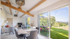 A modern interior with a dining area, a television, and a view of a green landscape through large glass doors. - Between Vineyards & the Sea | Beaches Within Walking Distance | Air Conditioning & Wi-Fi (La Ciotat)