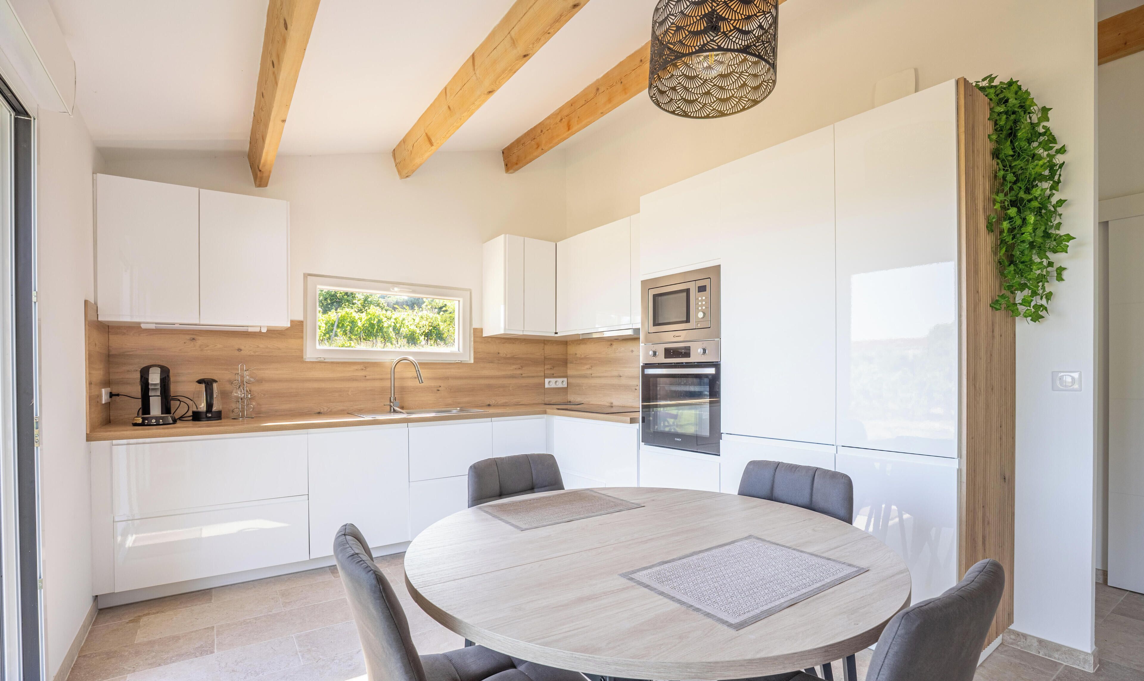A modern kitchen with white cabinets, a wooden countertop, a built-in oven, and a dining area with a round table and chairs.