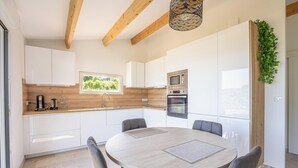 A modern kitchen with white cabinets, a wooden countertop, a built-in oven, and a dining area with a round table and chairs. - Between Vineyards & the Sea | Beaches Within Walking Distance | Air Conditioning & Wi-Fi (La Ciotat)
