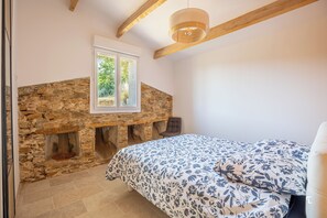 Ein Schlafzimmer mit Kamin aus Stein, einem Bett mit blumigem Bettzeug und einem Holzbalken an der Decke.