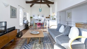Amplia sala de estar con sofá, televisión, mesa de comedor y cocina al fondo.