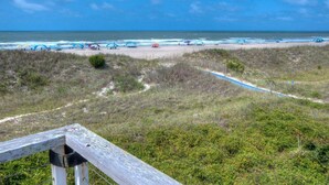 Een strand met een houten looppad naar het water, een hek en een helder uitzicht op de oceaan.