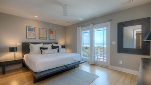 Een moderne slaapkamer met een groot bed, een plafondventilator, uitzicht door de glazen deur en kunst aan de muur.